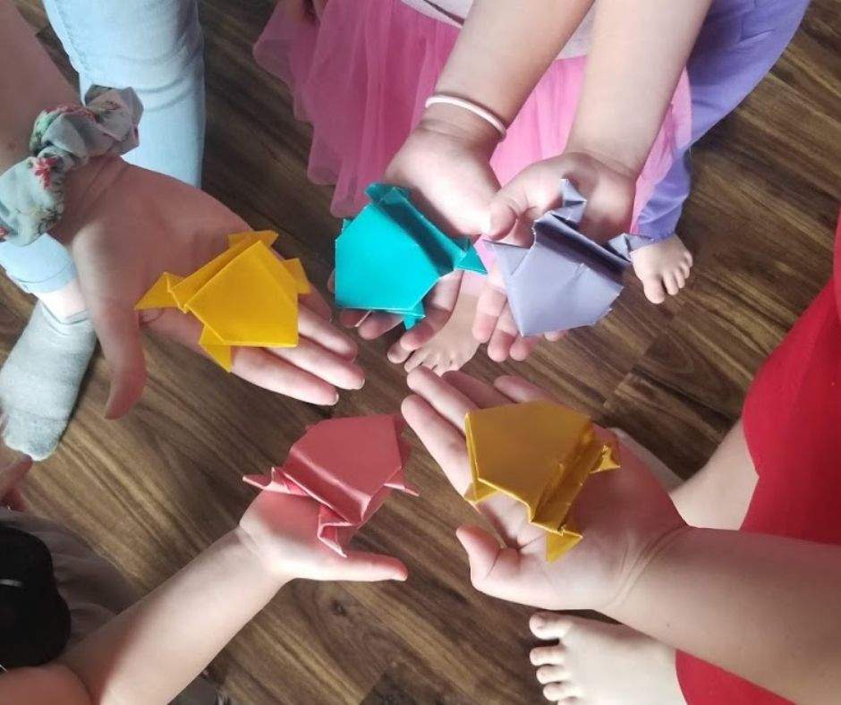 five hands holding origami frogs in a circle