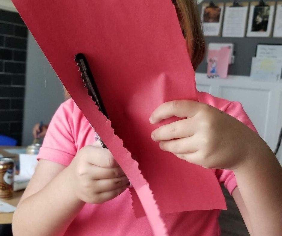 Girl using decorative scissors to make an edge on a strip of red construction paper
